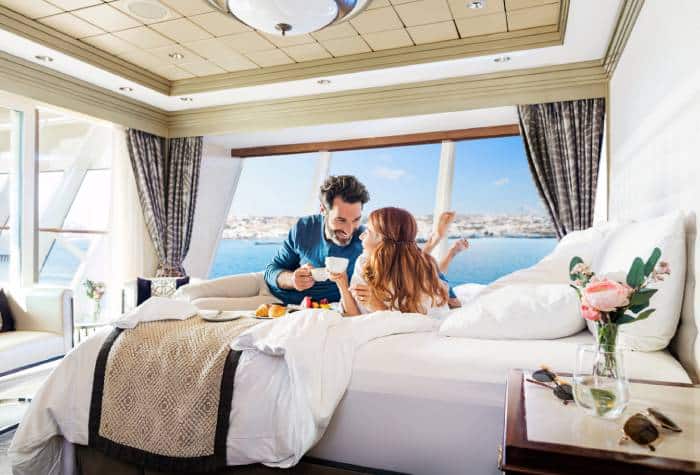 A couple enjoying a drink in their Norwegian bedroom Garden Villa onboard their cruise ship.