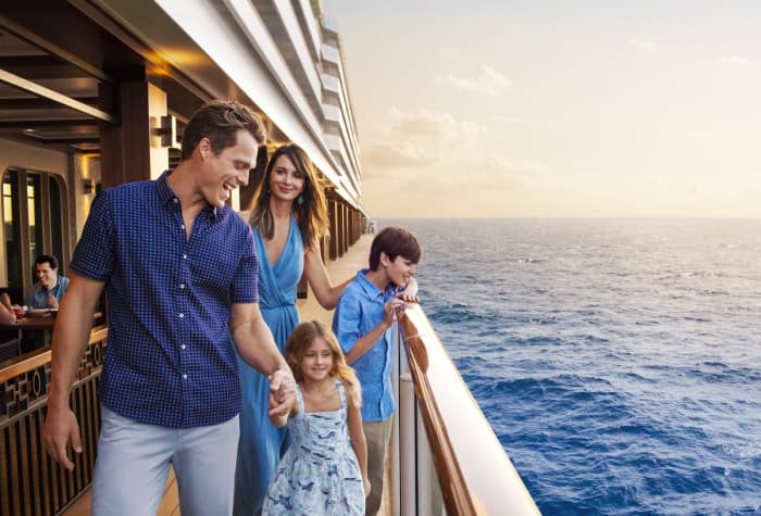 Family of 4 strolling along the boardwalk of Norwegian Escape cruise ship looking at the calm ocean